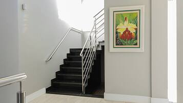 Una escalera con barandilla de metal, un rellano con alfombra negra y un cuadro enmarcado de flores en la pared.