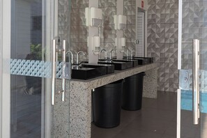 A modern bathroom with multiple sinks, a glass partition, and a geometric tile backsplash.