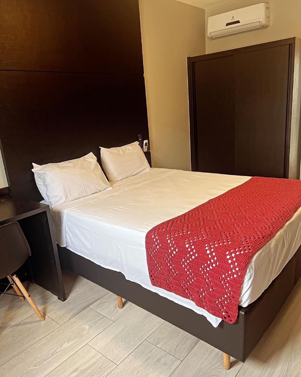 Una cama con colchón y almohadas blancas, una manta roja y un cabecero de madera.