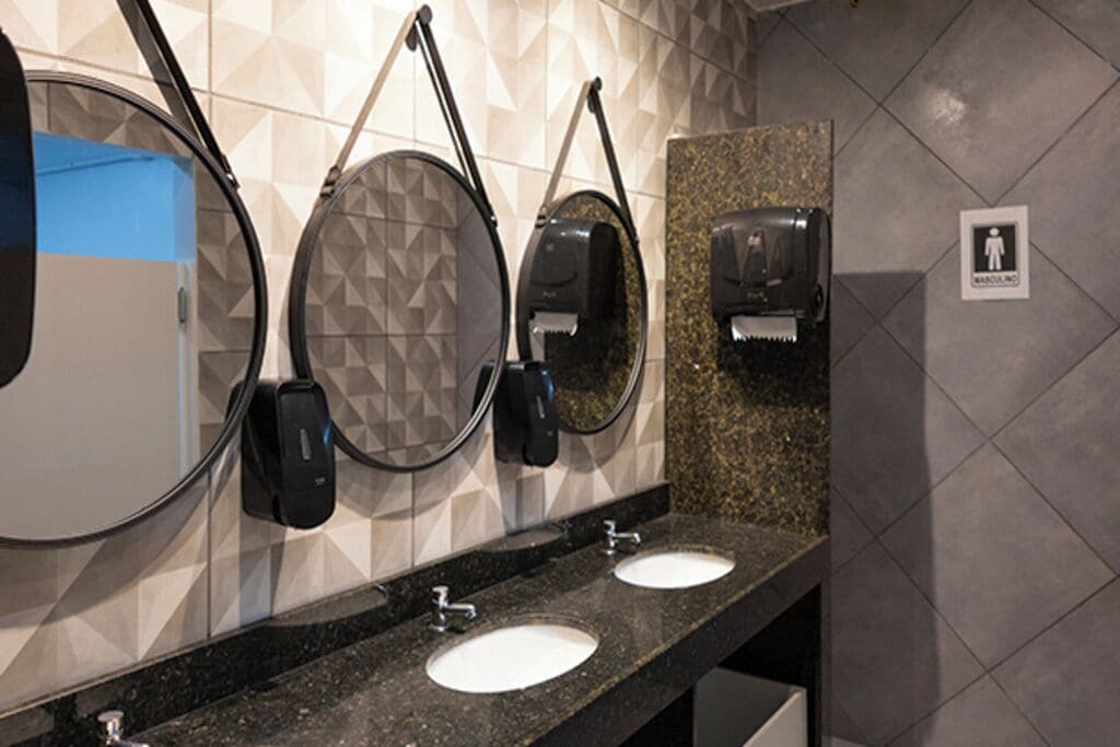 Un bagno pubblico con due lavandini, uno specchio e un asciugatore per le mani.