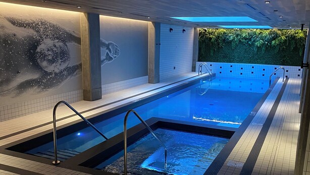 En moderne indendørs swimmingpool med fliset gulv, et håndaftryk-maleri og en grøn væg.