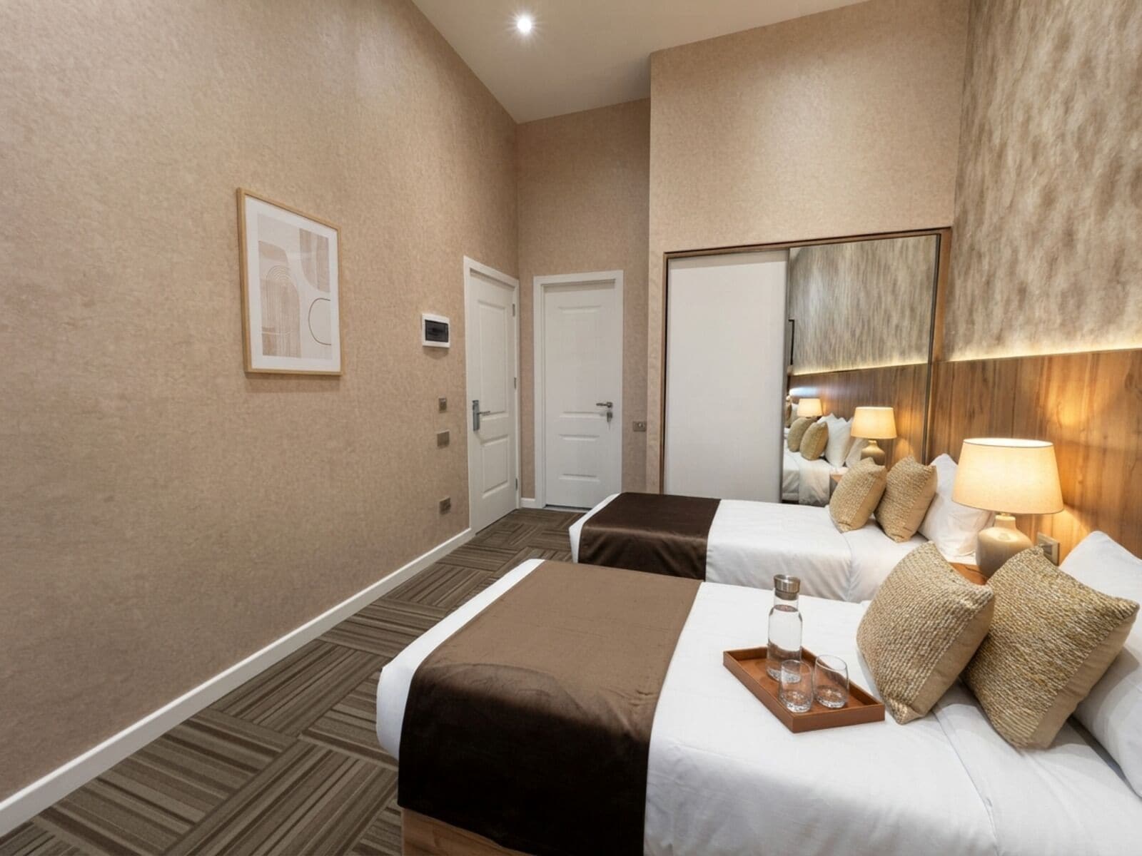 A hotel room with two beds, a large mirror, a door, and a carpeted floor.