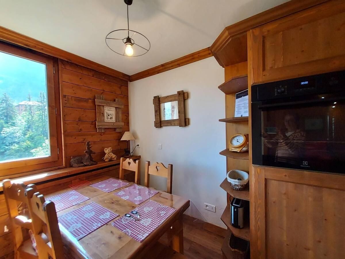 A wooden interior with a dining table, chairs, a television, and a window with a view of trees.