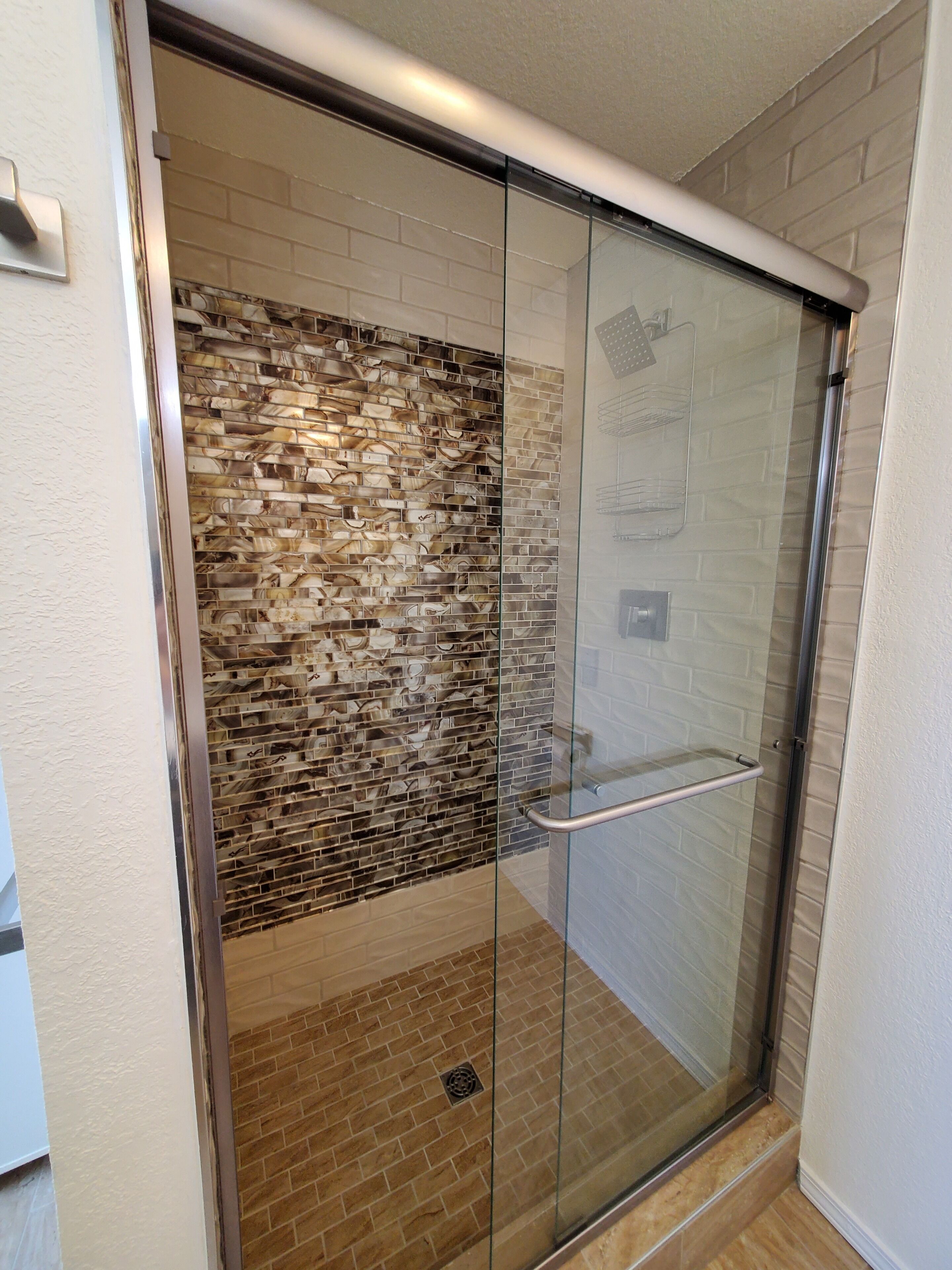 A glass-enclosed shower with a brick-patterned wall and a metal handrail.