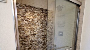 A glass-enclosed shower with a brick-patterned wall and a metal handrail.