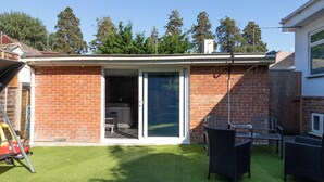 Ein Garten mit einer Terrassenfläche, einer Schaukel und einer Backsteinmauer.