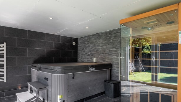 Ein moderner Wellnessbereich mit Whirlpool, einem kleinen Tisch und einer Glasumrandung mit Blick auf einen Garten.