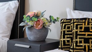 Ein Hotelzimmer mit Bett, Nachttisch, einer dekorativen Vase mit Blumen und einem gemusterten Kopfkissen.