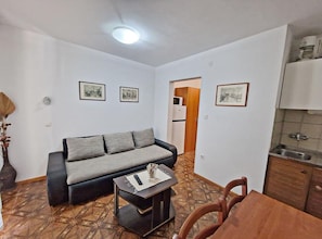 A compact living space with a sofa, a small table, a dining table, and a kitchenette. - Comfort One Bedroom Apartment with Terrace and Sea View (Pag)