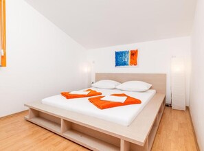 A modern bedroom with a wooden platform bed, white bedding, and orange towels. - Classic Two Bedroom Apartment with Terrace (Liznjan)