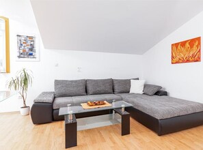 A modern living room with a sectional sofa, a glass coffee table, and a potted plant. - Classic Two Bedroom Apartment with Terrace (Liznjan)