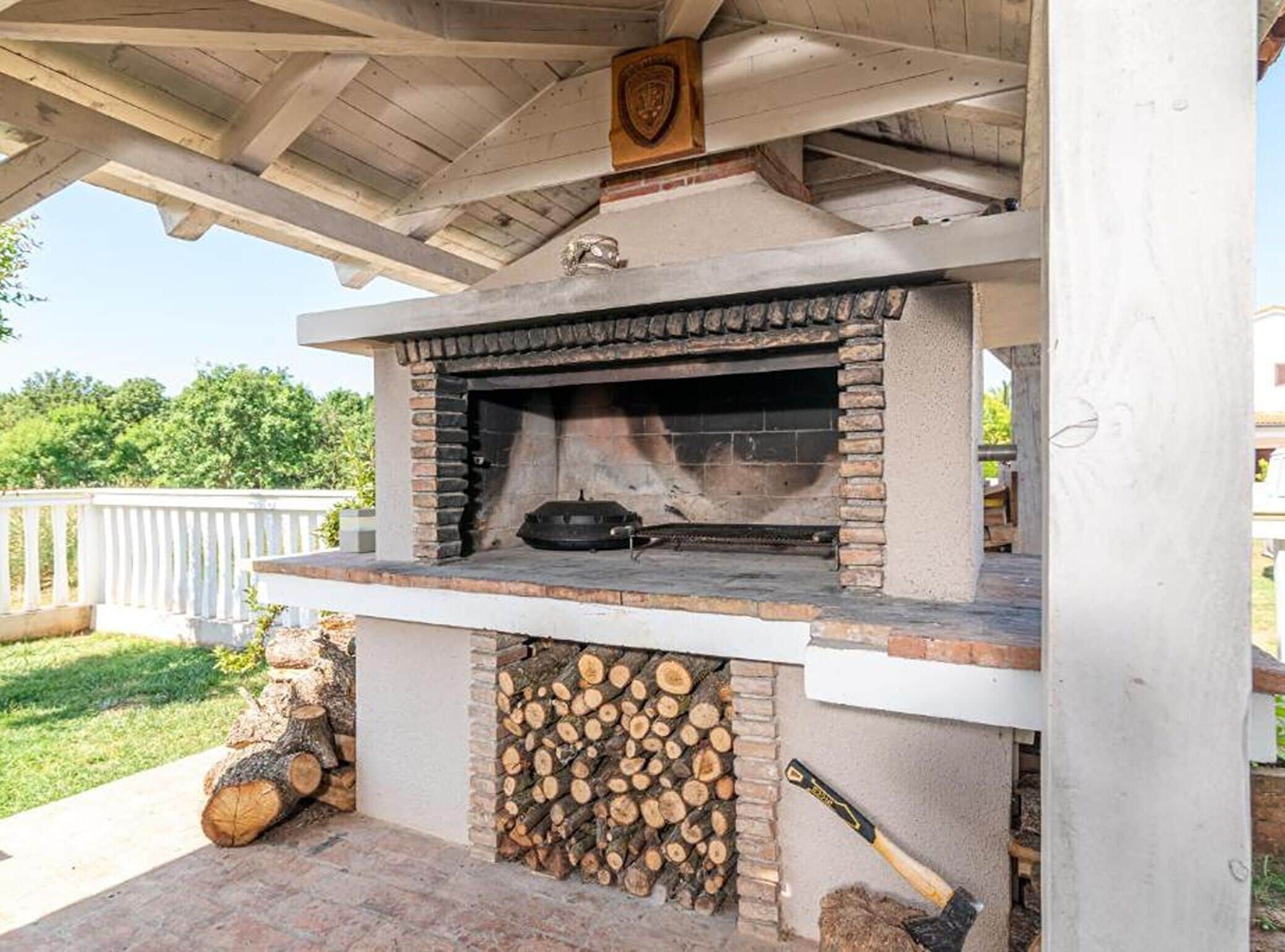 Ein Außenofen aus Ziegelsteinen mit Grill, umgeben von einer weißen Konstruktion mit Holzdach.