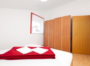 Ein Schlafzimmer mit einem Bett, einer roten Decke, einem Kleiderschrank und einem Fenster mit Jalousien.