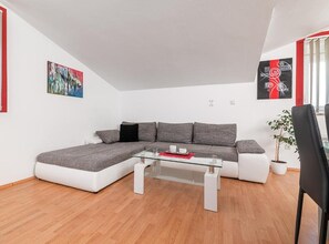 Ein modernes Wohnzimmer mit einem Ecksofa, einem Glastisch und einer Topfpflanze.