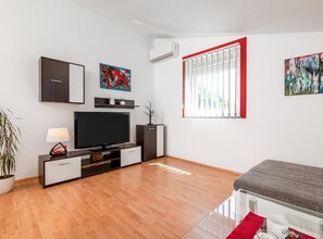 Ein modernes Wohnzimmer mit Flachbildfernseher, einer Couch, einem Couchtisch und einem Blumentopf.