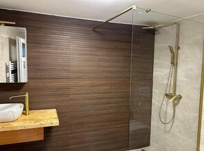 Ein modernes Badezimmer mit einer Holzvertäfelung, einer Duschkabine aus Glas und einem Holzwaschtisch mit weißem Waschbecken.