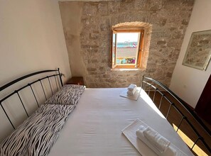A bedroom with a stone wall, a window with a view, a bed with a zebra-patterned pillow, and a metal headboard. - Three Bedroom Apartment with Sea View (Loviste)
