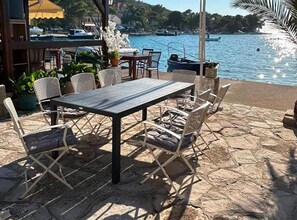 Ein Sitzbereich im Freien mit Tisch und Stühlen, mit Blick auf ein Gewässer und Boote.