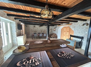 A rustic interior with stone walls, wooden beams, a dining area with a table and chairs, and a coffee-themed table runner. - Three Bedroom Apartment with Sea View (Loviste)