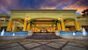 Ein Hotel mit einem imposanten Bogenportal, Stufen, die davor hinaufführen, und einem Springbrunnen im Vordergrund.