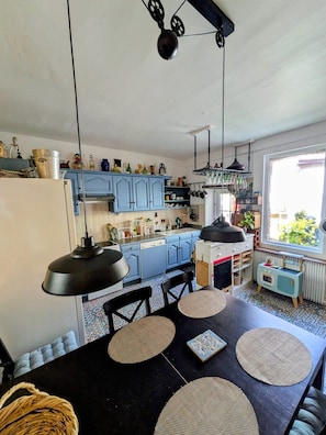 A kitchen with blue cabinets, a black table with woven placemats, and a hanging light fixture. - Artist's house · Terrace · Fécamp · Sleeps 4 (Fécamp)
