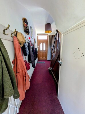 A hallway with a red carpet, a coat rack with various jackets, a door at the end, and a ceiling light. - Artist's house · Terrace · Fécamp · Sleeps 4 (Fécamp)
