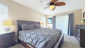 Una camera da letto con un letto, un comodino, una cassettiera, una ventola a soffitto e una finestra con tende.