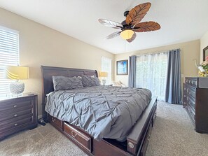 Ein Schlafzimmer mit Bett, Nachttisch, Kommode, Deckenventilator und einem Fenster mit Vorhängen.