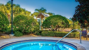 Una piscina con bordo piastrellato, circondata da vegetazione e un gazebo.