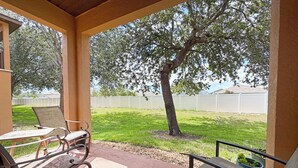 Un patio coperto con due sedie in metallo e un tavolo, un albero sullo sfondo e un recinto bianco.