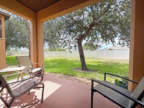 Ein überdachter Patio-Bereich mit zwei Metallstühlen und einem Tisch, ein Baum im Hintergrund und ein weißer Zaun.