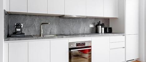 Una cocina moderna con armarios blancos, horno integrado y encimera de mármol.