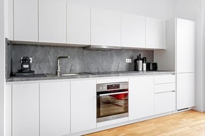 Uma cozinha moderna com armários brancos, forno embutido e bancada de mármore.