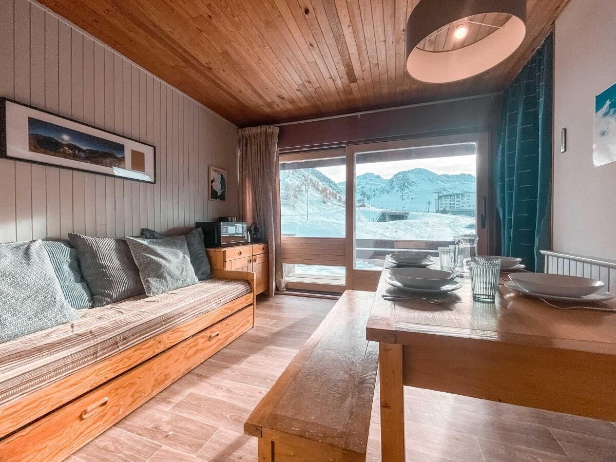 A wooden interior with a sofa, a dining table, and a view of snowy mountains.