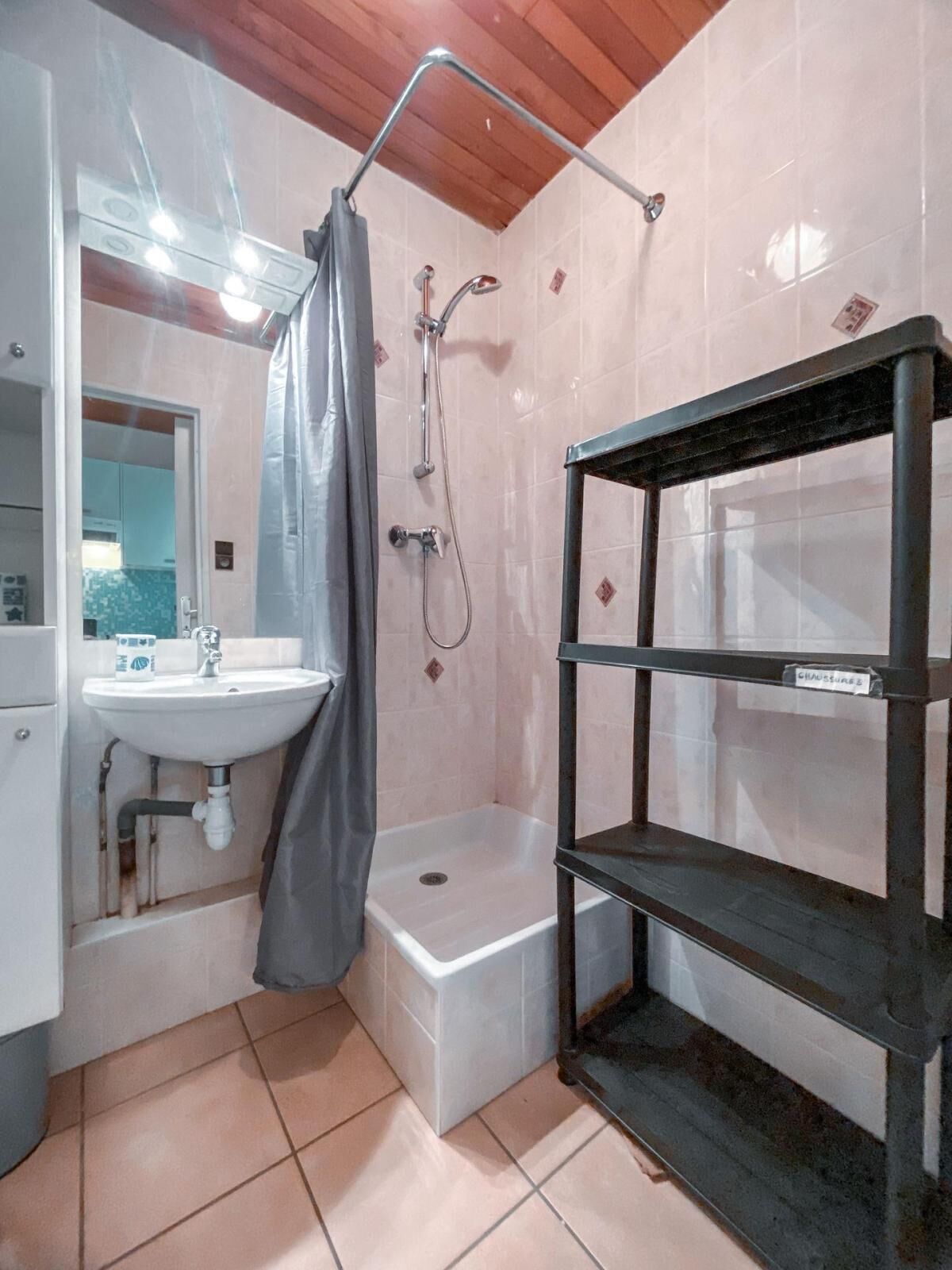 A bathroom with a white sink, a shower with a shower curtain, a bathtub, and a black shelf unit.