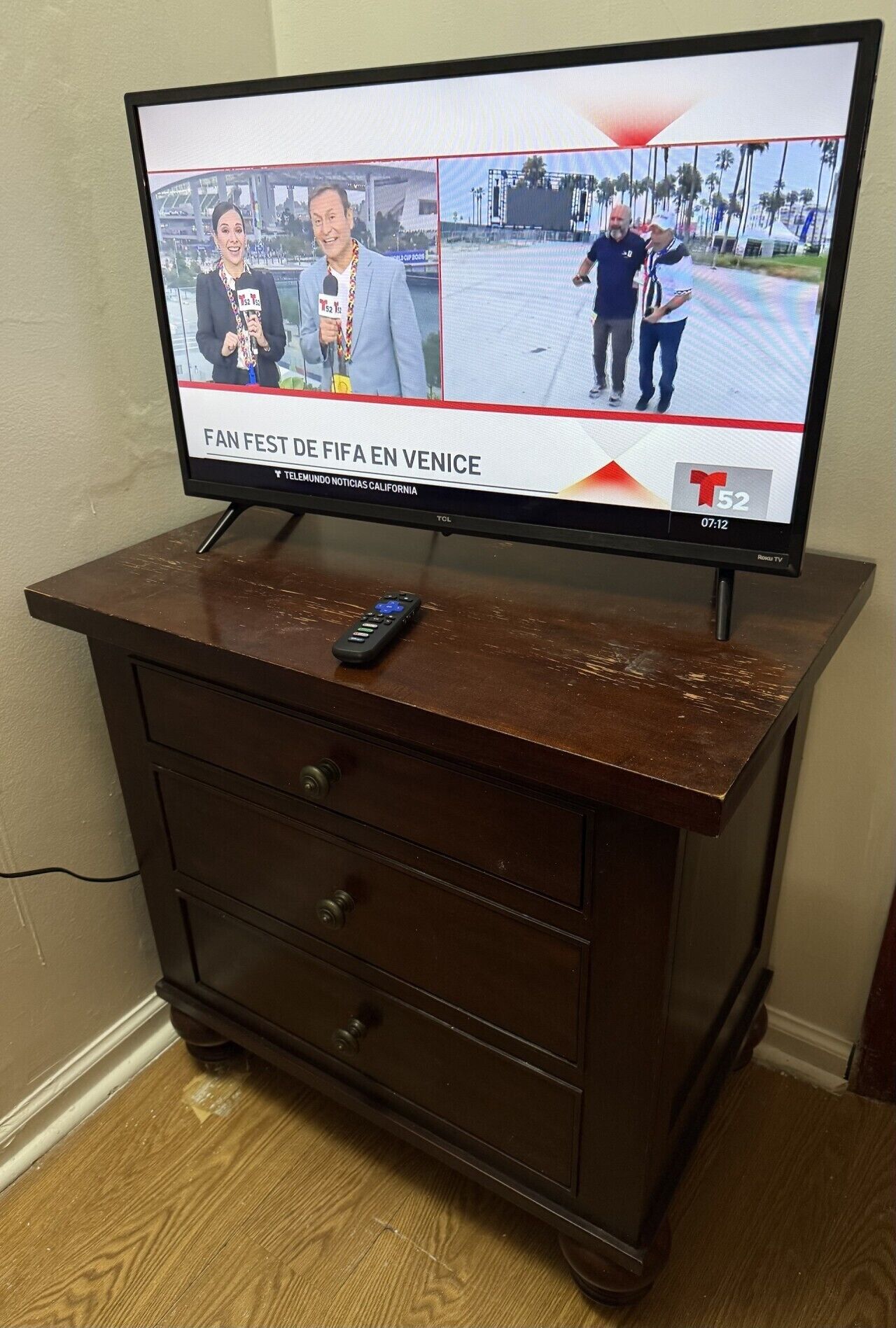 Ein Fernseher auf einer Holzkommode, ein Fernbedienung liegt obenauf.