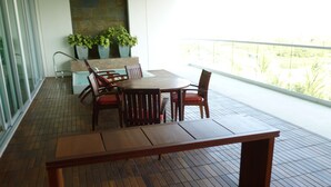 Una mesa y sillas de madera en un balcón con suelo de baldosas, pared de piedra y plantas en macetas.