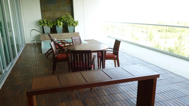 Una mesa y sillas de madera en un balcón con suelo de baldosas, pared de piedra y plantas en macetas.