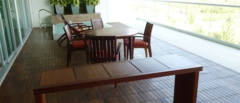 A wooden table and chairs on a balcony with a tiled floor, a stone wall, and potted plants.