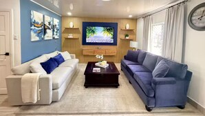 Una sala de estar con televisor, dos sofás, una mesa de centro y decoración en la pared.