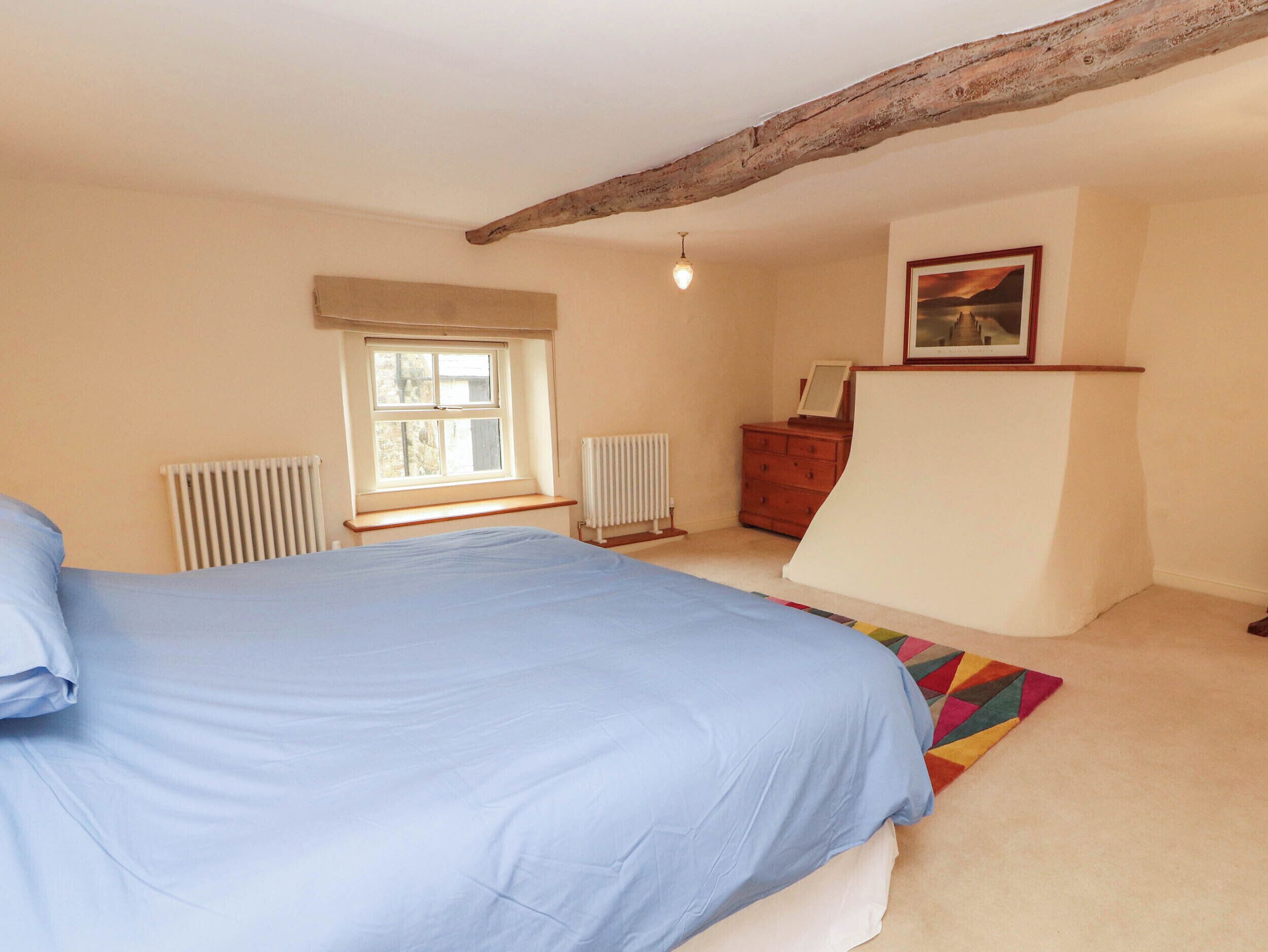 A bedroom with a bed, a radiator, a dresser, a window, and a picture on the wall.