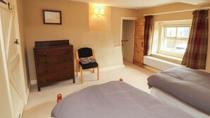 A bedroom with two beds, a dresser, a chair, a radiator, and a window with curtains. - Claybottom Farm (Wigton)