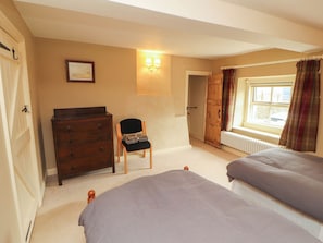 A bedroom with two beds, a dresser, a chair, a radiator, and a window with curtains. - Claybottom Farm (Wigton)