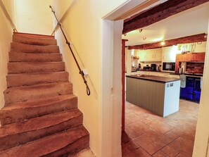 Eine Treppe führt zu einer Küche mit einer zentralen Kochinsel, Holzbalken und einem Fliesenboden.