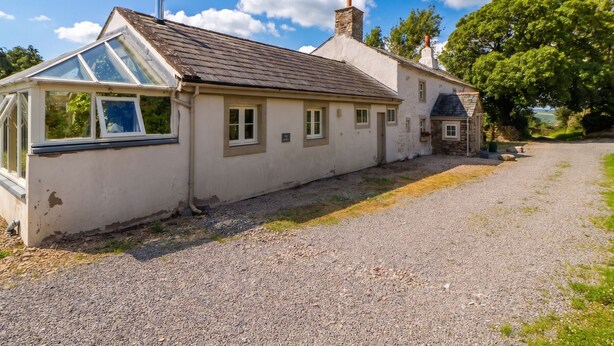 A single-story house with a sloped roof, a conservatory, and a gravel driveway. - Claybottom Farm (Wigton)