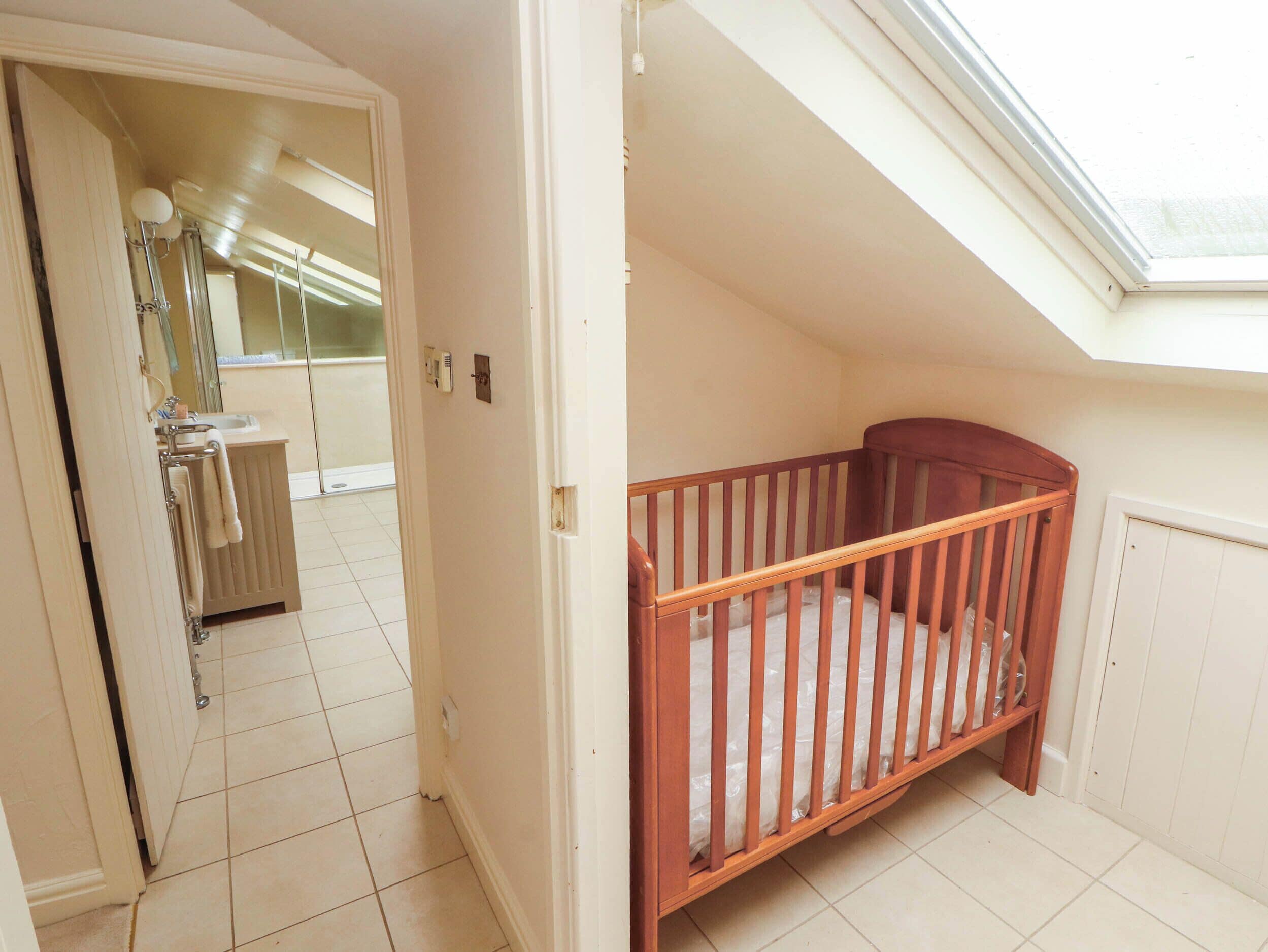 A room with a wooden crib, a skylight, a bathroom with a sink and mirror, and a tiled floor.