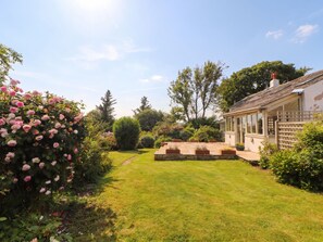 Ein gepflegter Garten mit Rasenfläche, Blumenbeeten und einem Gebäude mit großen Fenstern.