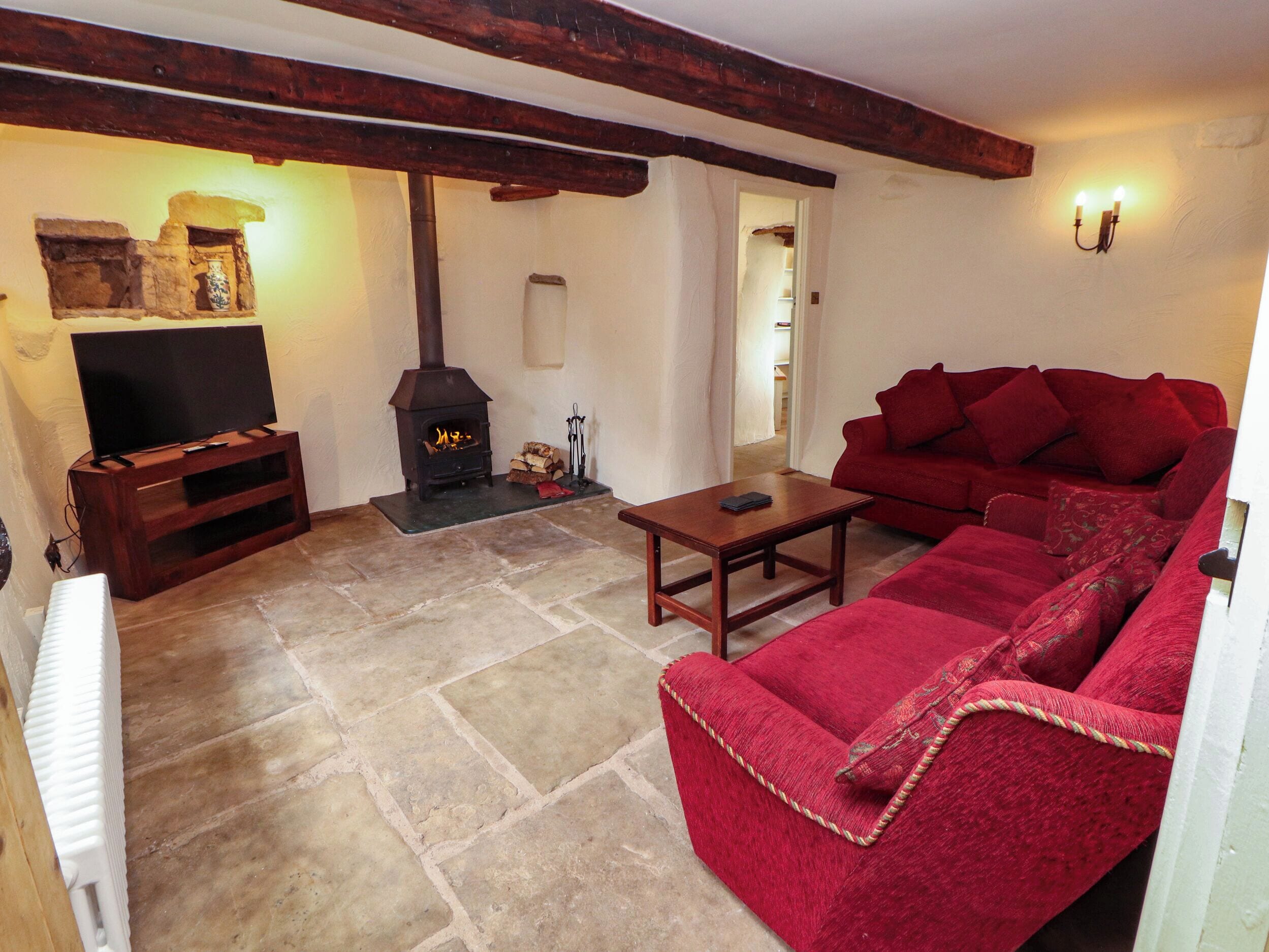 Una sala de estar acogedora con piso de piedra, un sofá rojo, una mesa de centro de madera, un televisor sobre un mueble de madera y una chimenea.