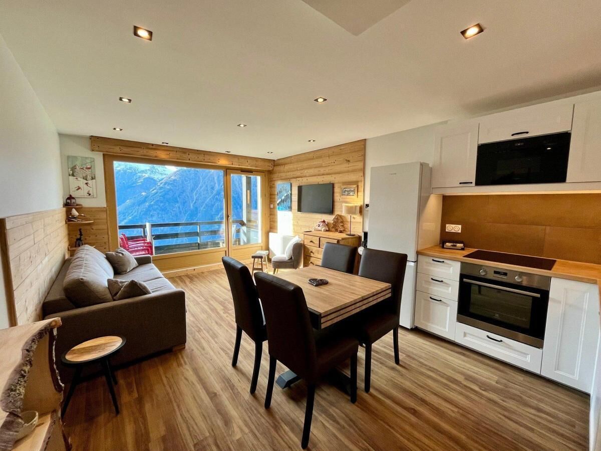 A modern interior with a dining area, sofa, kitchen, and large windows offering a mountain view.