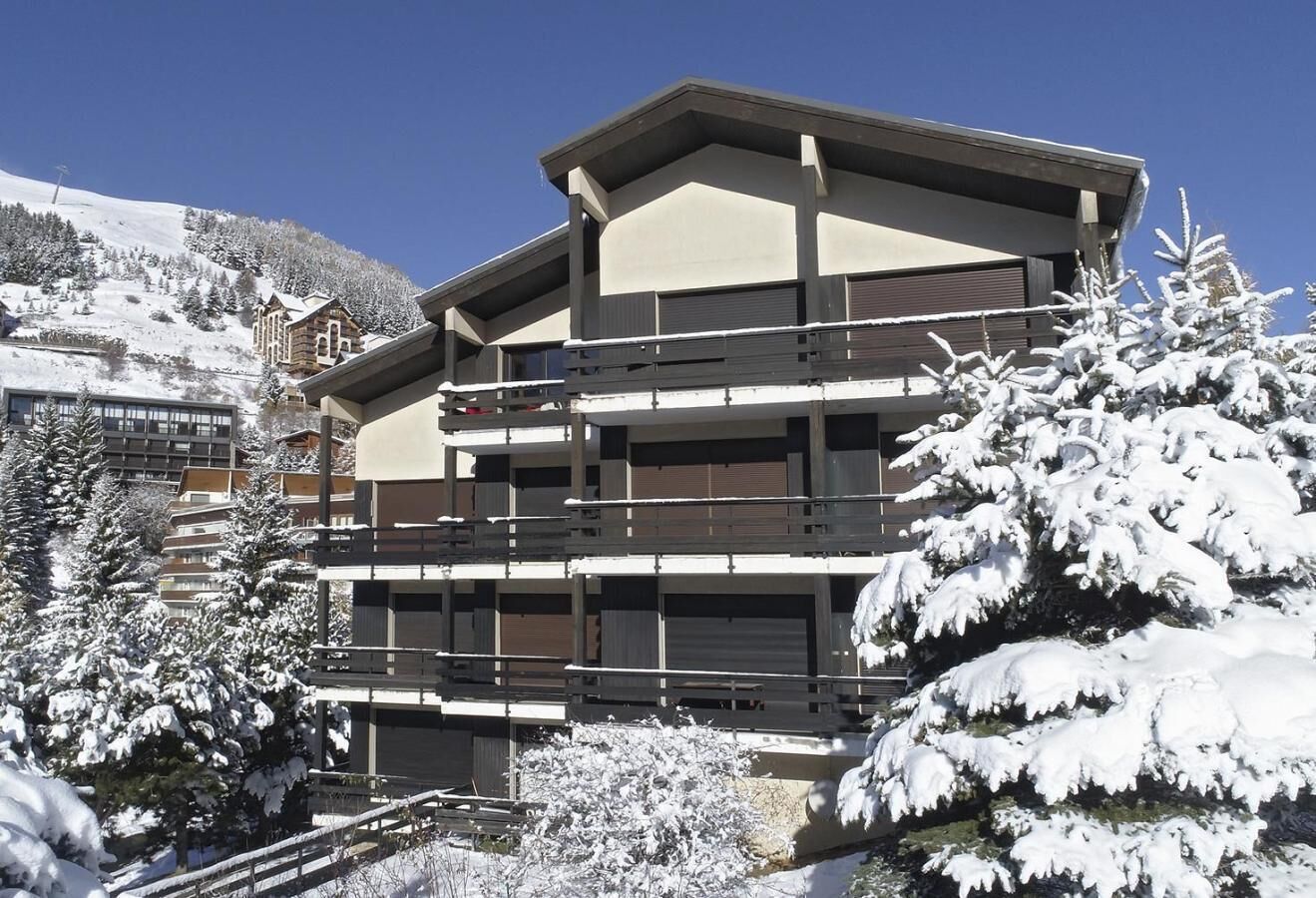A multi-story building with balconies, surrounded by snow-covered trees and a mountain in the background.